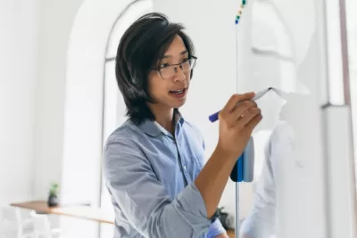 homem asiatico concentrado em camisa azul usando flipchart e marcador para o trabalho